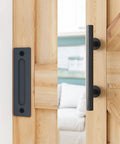 All In One Heavy Duty Sliding Barn Door Hardware Kit Features 11 Foot Track With Whisper Quiet Nylon Rollers For Rock Solid Reliability Smooth Silent Operation Dead Simple Install Durable Alloy Frame No Door Included Matte Black Finish close-up of matte black door handle and plate on wood barn door.