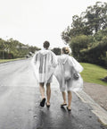 Two adults wearing disposable rain ponchos for adults six pack with drawstring hood lightweight and fifty percent thicker material.