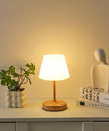 Cordless LED Wood-Grain Table Lamp With Waterproof Shower Design illuminating on table with books and plant, cozy ambience