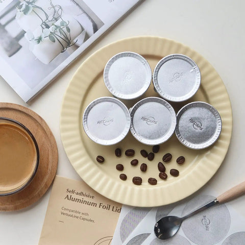 Plate displaying Aluminum Foil Lids for Reusable Coffee Pods, 62mm Seals for Nespresso VertuoLine, with coffee beans and drink