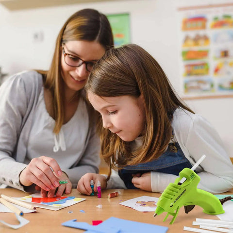 Mother and daughter crafting with Cool Shot Ultra Low Temp 4 Inch Mini Glue Sticks Pack For Delicate Materials Like Balloons Ribbon Lace Fabric And Foam Crafts DIY Friendly 15 Count Ideal For Low Temp Glue Guns in a classroom setting