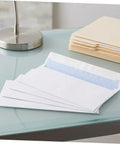 White Pro-Grade Self-Sealing Security Mailing Envelopes 115mm X 225mm shown open on a glass desk with folders