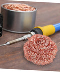 Soldering iron next to Six Pack Soldering Tip Copper Wire Sponge Balls for efficient tin removal on a wooden surface.