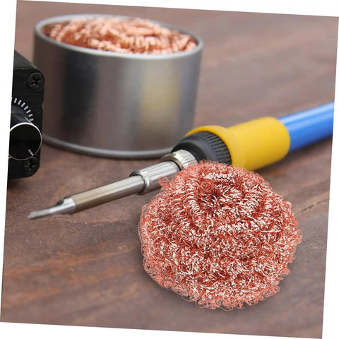 Soldering iron next to Six Pack Soldering Tip Copper Wire Sponge Balls for efficient tin removal on a wooden surface.