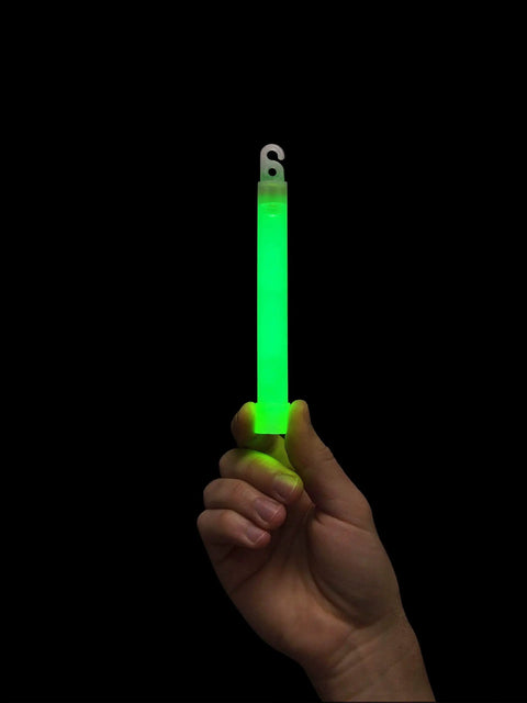 Hand holding a Beefed Up Military Grade Green Glow Stick 6 Inch Snap Light Emergency Chemical Light 12 Hour Duration for outdoor use.