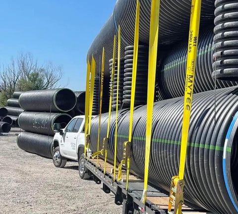 Hella Tough Ratchet Tie Down Straps With Flat Hooks securing large pipes in transport, 30ft long yellow polyester webbing.