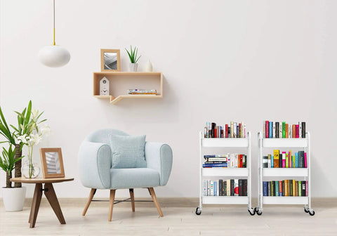 Two Three Tier Rolling Metal Storage Organizer On Wheels White Mobile Utility Cart With Caster Wheels For Kitchen Office Home And Garage Organization Durable Powder Coated Steel Mesh Baskets filled with books next to a modern armchair and small table in a living room.