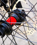 Close-up of a mountain bike wheel hub with a red accent, featuring the Complete Mechanical Disc Brake System For Mountain Bike Front And Rear With Forged Aluminum Calipers And Long Wear Pads That Give You Dang Serious Stopping Power On Gnarly Downhills Without Breaking The Bank.