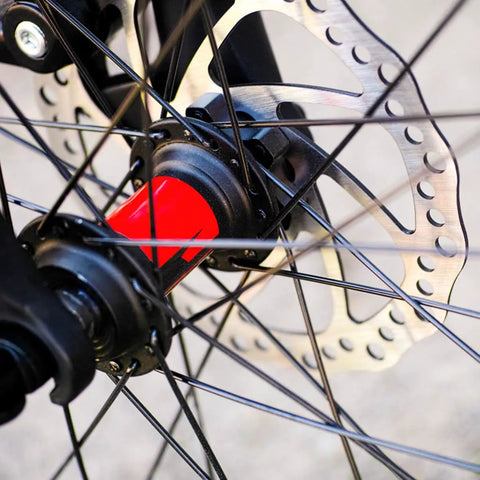 Close-up of a mountain bike wheel hub with a red accent, featuring the Complete Mechanical Disc Brake System For Mountain Bike Front And Rear With Forged Aluminum Calipers And Long Wear Pads That Give You Dang Serious Stopping Power On Gnarly Downhills Without Breaking The Bank.