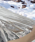 Person holding Emergency Mylar Thermal Blanket For Survival Kits And Outdoor Gear Rugged Heat Retention Hypothermia Prevention 100 Pack Silver.