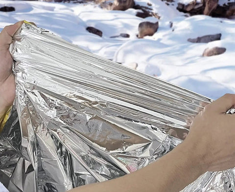 Person holding Emergency Mylar Thermal Blanket For Survival Kits And Outdoor Gear Rugged Heat Retention Hypothermia Prevention 100 Pack Silver.