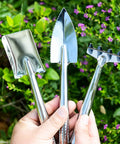 Three Piece Mini Garden Tools Set with stainless steel triangle shovel, square transplant spade, and hand rake held in hand