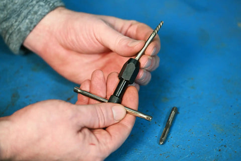 Hands holding T Handle Tap Wrench 1/4 Inch For Easy Tap Install And Precise Threading tool against blue background