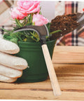 Portable Manganese Weeding Sickle with Non Slip Handle for gardening near pink flower in pot.