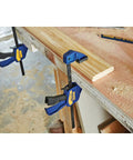 Six Inch Mini Bar Clamp Two Pack With One Hand Quick Release Trigger on wood, demonstrating firm grip and non-marring pads.