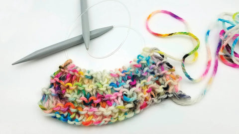 Knitted swatch on circular knitting needles with multicolor variegated yarn on white background