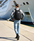 Person wearing Military Tactical Backpack With Laser Cut MOLLE Webbing, 25L EDC Daypack For Men, near a docked ship.