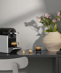 Pixie Aluminum Espresso Machine For Capsule Coffee Lovers on a countertop, brewing espresso, beside a vase of flowers.