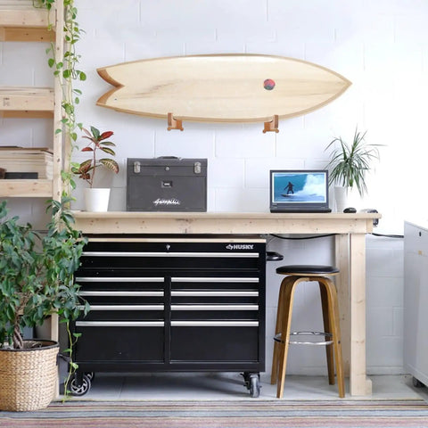 Premium Spliced Beech Wood Surfboard Wall Mount Rack Vertical Storage Shelf For Shortboards Longboards And Skimboards with surfboard above workspace.