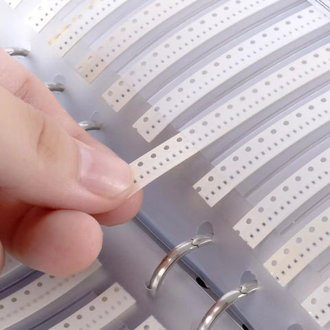 Ultimate 0402 SMD Resistors Kit With 170 Values, 50 Pieces Each, in a booklet, being handled delicately with fingers.