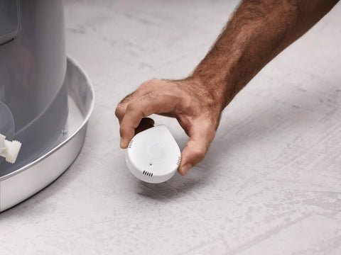 Person placing Flo Smart Water Leak Detector 3 Pack near washing machine for real-time alerts and monitoring.