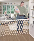 Extra Wide Swing Out Wooden Baby Gate Fits Twenty Four To Sixty Inch Openings Super Secure With Safety Latch And Hardware Mount Thirty Two Inches Tall Sustainable Hardwood For Homes With Kids And Pets shown installed in a bright living room with a dad holding a baby and mom watching on sofa.