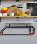 Hacksaw with black and red handle mounted on a wall holder with shelf above containing paint and art supplies.