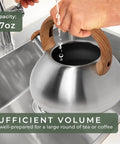 Filling stainless steel stovetop whistling tea kettle 2.4 qt with water, showing capacity, wood handle, sink view