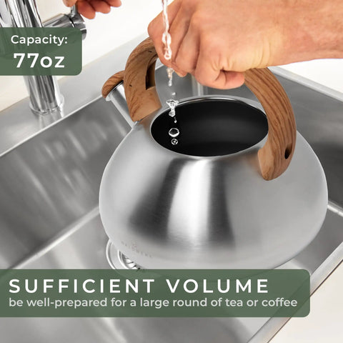 Filling stainless steel stovetop whistling tea kettle 2.4 qt with water, showing capacity, wood handle, sink view