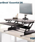 Two Tier Standing Desk Converter With Dual Handle Lift For Monitors And Accessories, 36 Inch Wide Sit Stand Riser, shown in an office