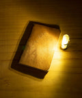 Aurora A7 G4 Keychain Flashlight USB C Rechargeable 650 Lumen EDC Light illuminating a wooden notebook, glow blue for camping emergencies.