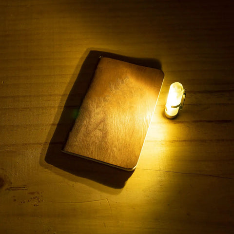 Aurora A7 G4 Keychain Flashlight USB C Rechargeable 650 Lumen EDC Light illuminating a wooden notebook, glow blue for camping emergencies.