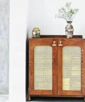 Wooden cabinet with woven door panels, adorned with floral vases on top, standing against a white wall.