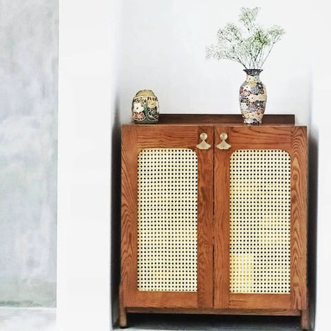 Wooden cabinet with woven door panels, adorned with floral vases on top, standing against a white wall.