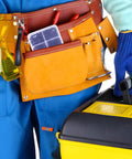 Person in blue coveralls with a tool belt carrying a yellow toolbox