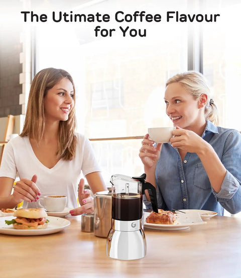 Two women enjoying coffee with Stovetop Moka Pot For 9 Cups Espresso Maker 15oz Italian Coffee Clear Glass And Stainless Steel Base on table.