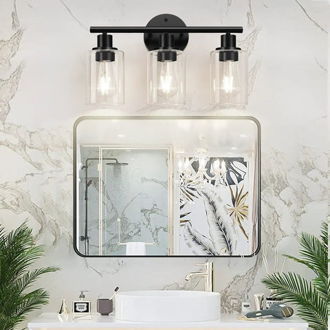 Image of Three Light Matte Black Bathroom Vanity Light Fixtures with Clear Glass Shades installed over a mirror in a bathroom.