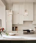 One Light Mini Pendant In Brushed Nickel hanging over modern kitchen island with white cabinets and flowers