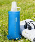 Blue foldable soft water bottle that is leakproof and packable for travel hikes and camping, 250ml size, resting on a towel in grass.