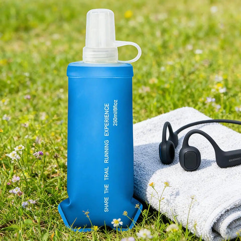 Blue foldable soft water bottle that is leakproof and packable for travel hikes and camping, 250ml size, resting on a towel in grass.