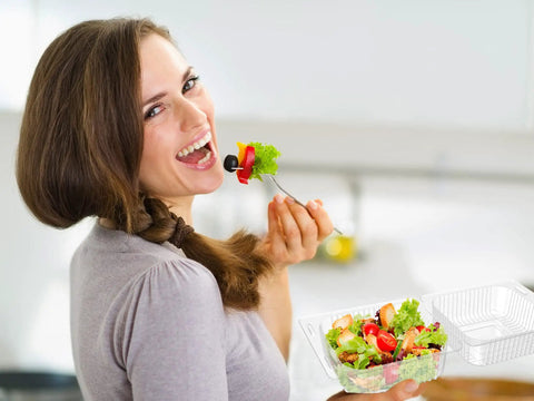 Smiling person holding a salad in a clear plastic hinged takeout clamshell container, showcasing its easy-to-use design.