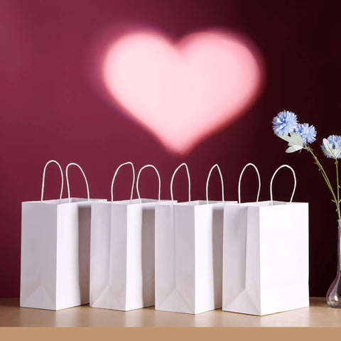 White Kraft Paper Gift Bags With Handles Pack Of 25 Medium 8 By 4.5 By 10 Inches on display against a heart backdrop.