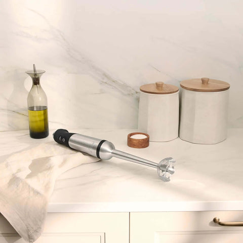 Heavy Duty Stainless Steel Immersion Blender With Kickass 600 Watt Motor And Turbo Switch on countertop beside containers.