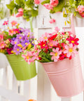 Pink hanging flower pot with artificial daisies on a white fence, decorative garden display