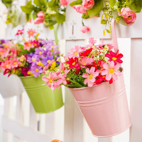 Pink hanging flower pot with artificial daisies on a white fence, decorative garden display