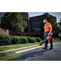 Man using M18 FUEL Cordless Handheld Blower With 120 MPH Air, 450 CFM, outside on pavement, red and black, light cleanup