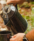Pouring hot beverage from 3 Qt Coffee Boiler In Speckled Black For Quick Brews, Rapid Heat Absorption, Holds Up To 12 Cups, Easy Pour Spout