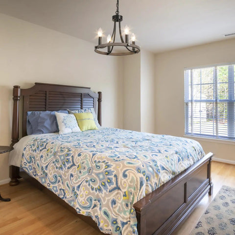 Wagon Wheel Black Farmhouse Chandelier With 4 Lights illuminating a cozy bedroom, featuring rustic decor and wooden bed.
