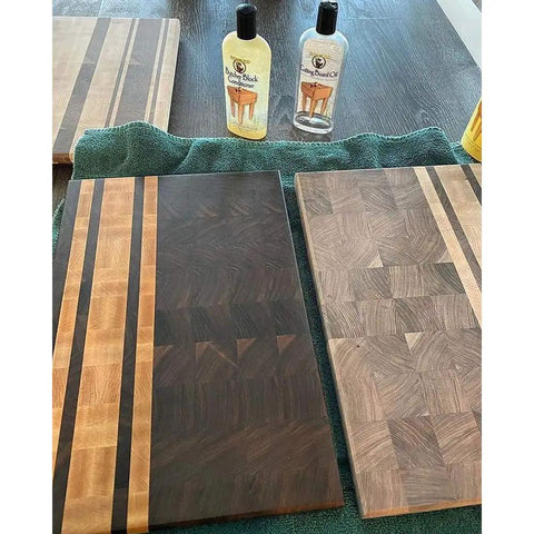 Two bottles of Heavy-Duty Go-To Butcher Block Conditioner and Cutting Board Oil, 12 oz, next to wooden cutting boards on a table.