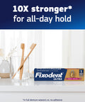 Fixodent Ultra Max Hold Denture Adhesive Cream box on bathroom counter with toothbrushes, 10X stronger all-day hold claim.